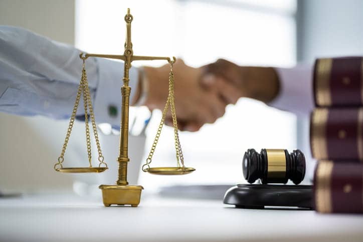 A Personal Injury Attorney Is Discussing A Case With A Client As He Writes In A Notebook. 