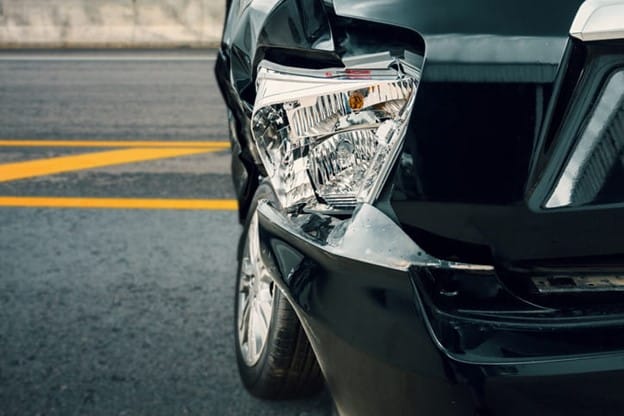 Types Of Auto Accident Claims 1 An Auto Accident Scene Featuring A Black Car With A Severely Damaged Front End And Broken Headlight On A Road.