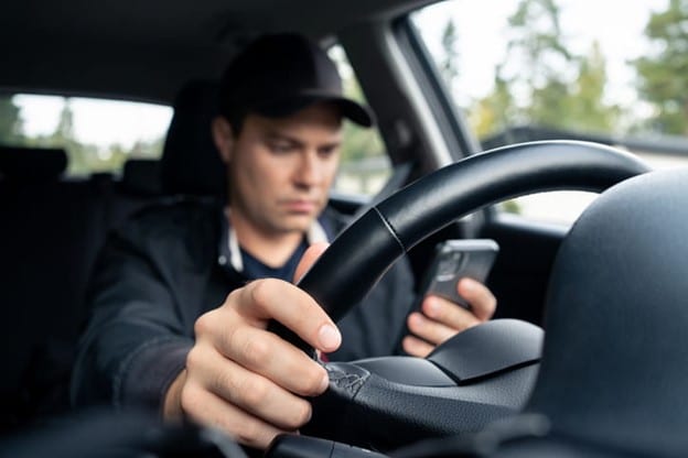 Reckless Driving 1 A Driver Engaging In Reckless Driving By Texting On A Smartphone While Steering With One Hand, Showcasing A Dangerous Distraction.