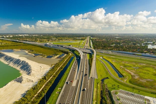 Miami Turnpike Accident Lawyer 1 An Aerial View Of A Turnpike Highway Interchange With Multiple Lanes, Overpasses, And Surrounding Green Landscapes Under A Partly Cloudy Sky.