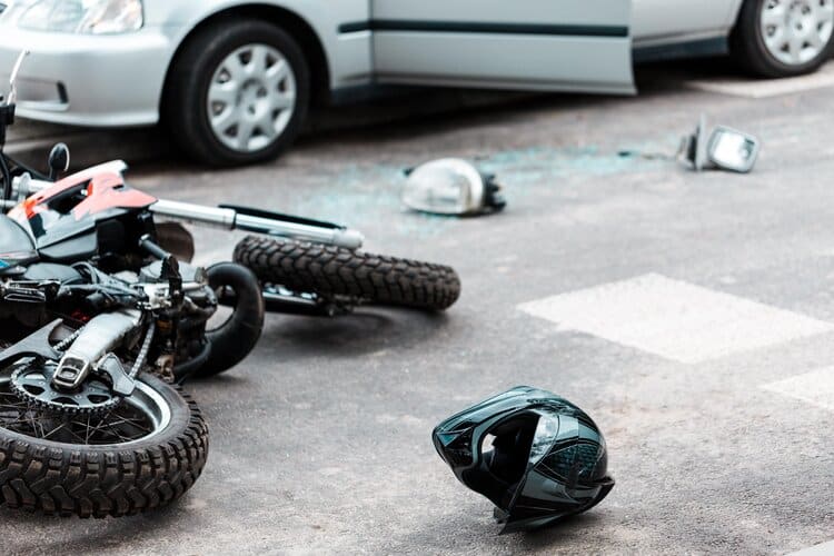 A Damaged Motorcycle Lies On The Road With Scattered Debris, A Helmet, And A Car Nearby After An Accident.