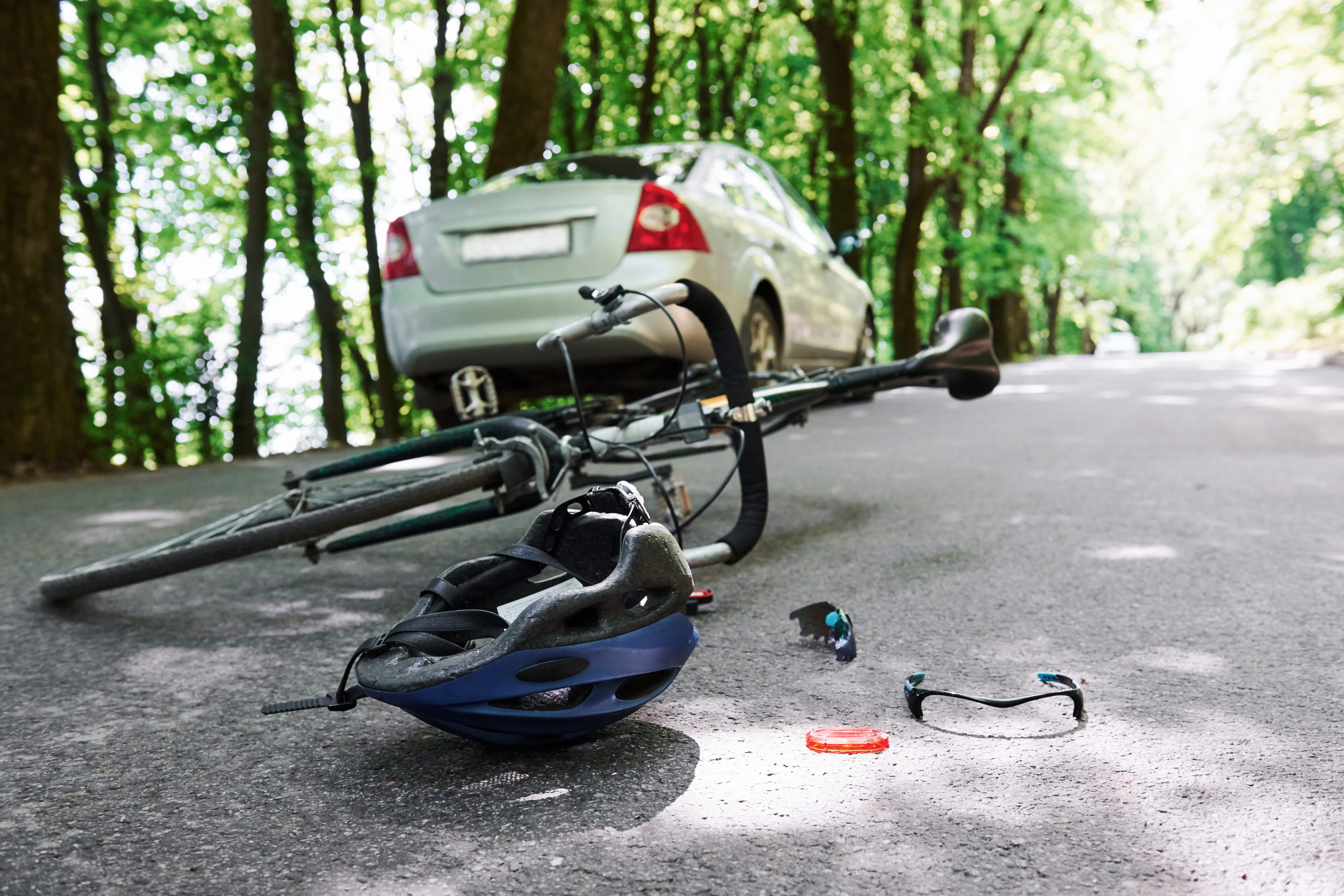 Bicycle accident with a car on a forest road showing a damaged bike, helmet, and broken glasses.