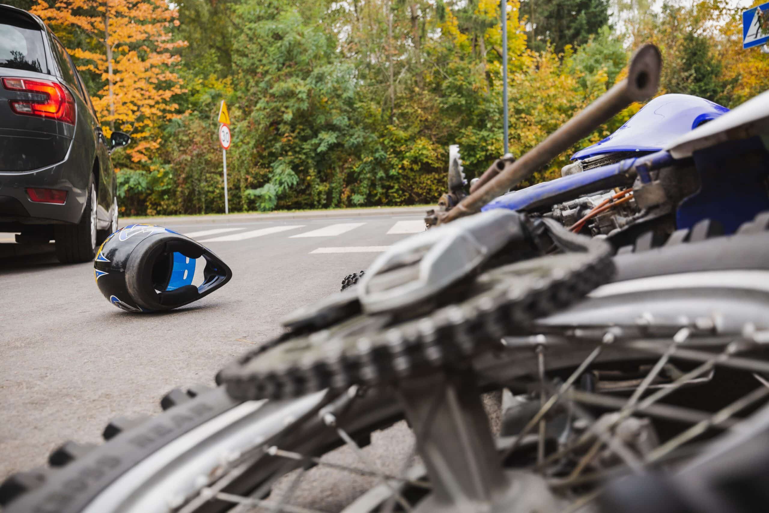 Damaged Motorcycle And Helmet On Road After Hit And Run Accident With Black Car In Background

