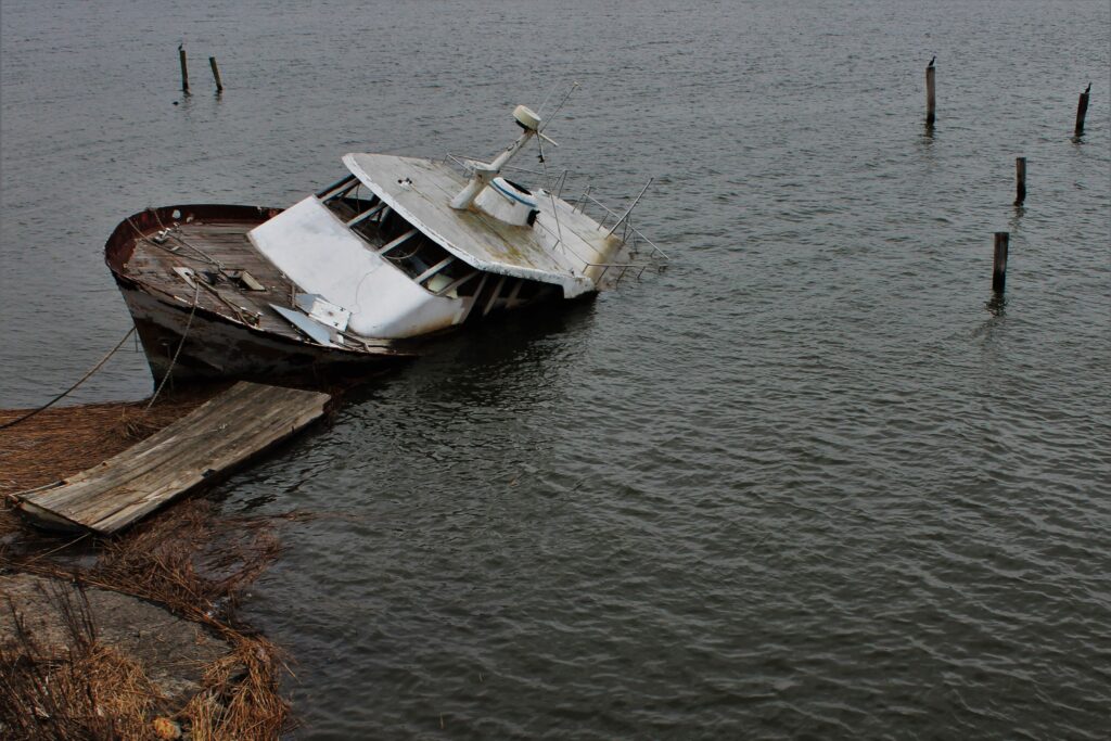 Boat Operator Responsibility After An Accident 1 Partially Sunken And Rusted Boat Near The Shore With A Wooden Ramp Leading To It, Illustrating Hazards In Maritime Rescue Operations.