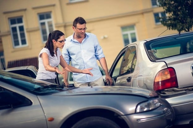 Parking Lot Accidents 1 Two People, A Man And A Woman, Gesturing While Discussing A Minor Accident Between Two Silver Cars In A Parking Lot, With Buildings And Trees In The Background.