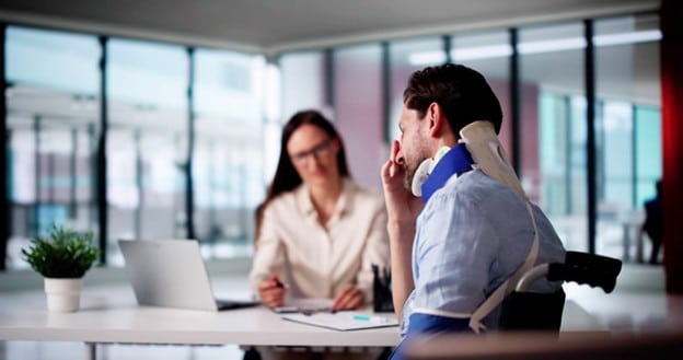 Miami Beach Personal Injury Lawyer 2 A Man Wearing A Cervical Neck Brace And Arm Sling Sitting Across From A Female Personal Injury Lawyer In A Modern Office With Large Windows, Discussing His Case While She Takes Notes.